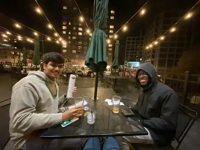 Two friends enjoying drinks at Dublin Square outdoor patio at night.