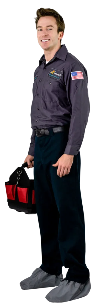 A friendly technician from Fetch‑A‑Tech, dressed in a professional uniform and protective shoe covers, stands in a Las Vegas home with a welcoming smile and reliable tool bag—ready to provide honest, helpful service that puts your comfort first.