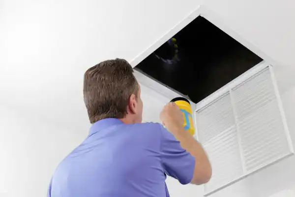 A friendly technician from Fetch‑A‑Tech, proudly serving Las Vegas, inspects an open ceiling vent with a flashlight in a bright, comfortable home. His careful attention reflects our family-owned team’s dedication to providing honest, helpful air duct repair and ensuring your comfort.