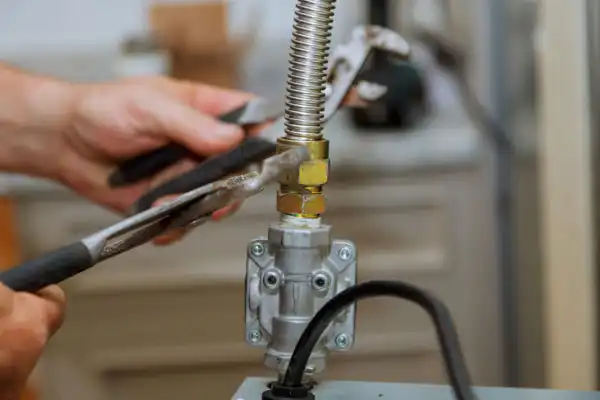 A skilled technician carefully uses two wrenches to secure a flexible metal gas line to an appliance fitting, ensuring a safe and comfortable home in Las Vegas. The scene reflects Fetch‑A‑Tech’s honest, family-owned service—always here to help your family with reliable expertise.