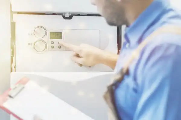 A friendly Fetch‑A‑Tech technician in a blue shirt and overalls adjusts the settings on a wall-mounted control panel, ensuring comfort in a Las Vegas home. The technician holds a clipboard, ready to help with honest, reliable service you can trust from our family-owned team.