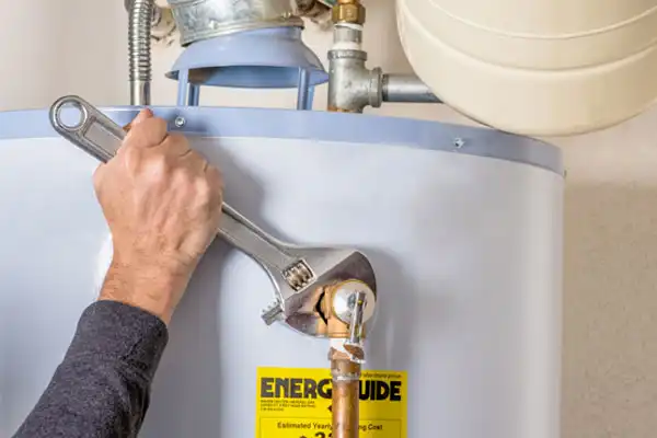 A friendly technician tightens a pipe fitting on top of a water heater—clearly marked with an EnergyGuide label—using a large adjustable wrench. Providing honest and helpful service in Las Vegas, Fetch‑A‑Tech ensures your home stays comfortable and energy-efficient.
