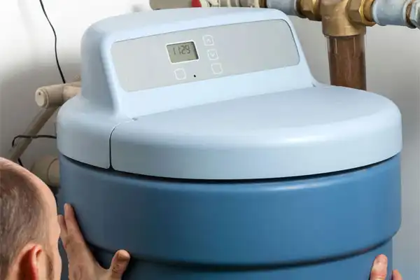 A friendly technician from Fetch‑A‑Tech inspects a blue water softener with an easy-to-read digital display, ensuring clean, comfortable water for a Las Vegas home. The technician’s careful work highlights our honest, family-owned commitment to your comfort and helpful service.