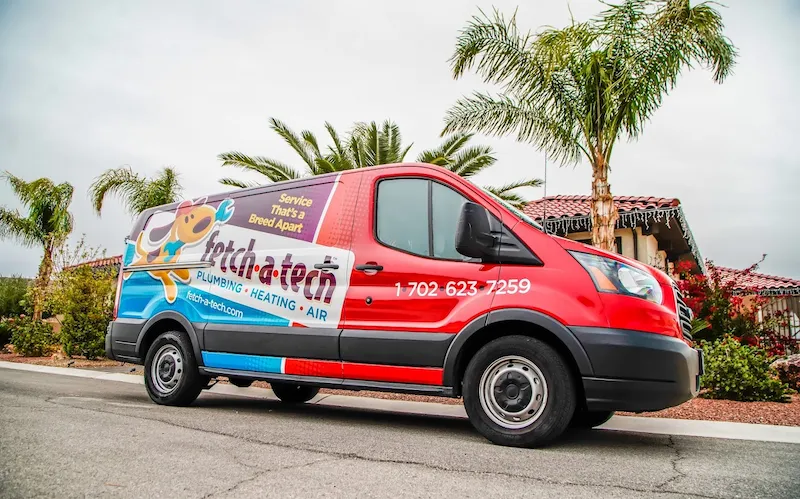 A friendly Fetch‑A‑Tech van, proudly displaying our signature red and blue colors, is parked on a welcoming Las Vegas neighborhood street lined with palm trees and family homes—ready to help with your plumbing, heating, or air needs.