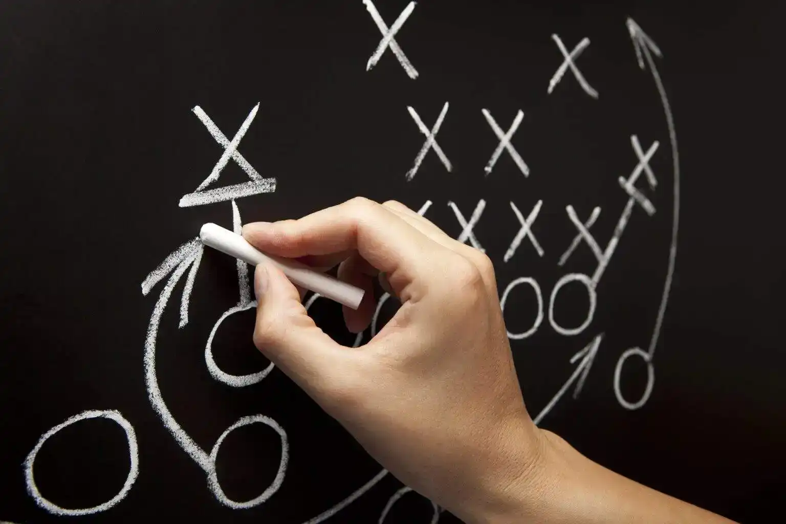 Man drawing a game strategy with white chalk on a blackboard.