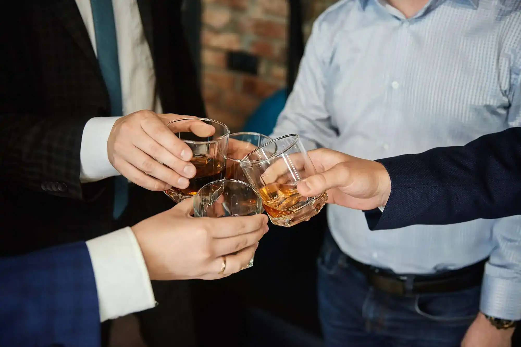 Group of four friends men in the whisky drink party holding glass of alcoholic beverages in their hands and clinking. Close up