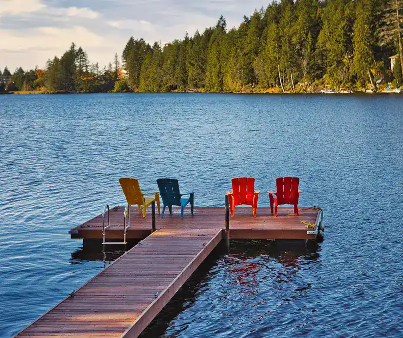 Beautiful lake dock with colorful Adirondack chairs overlooking tranquil water.
