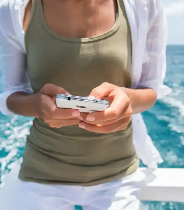 Close-up of woman using smartphone on boat at sea, enjoying outdoor water activities.