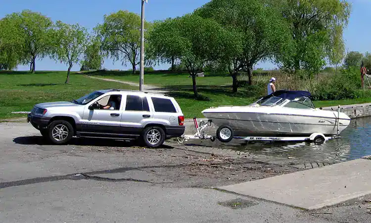 Bright image of a silver SUV towing a boat trailer near water.