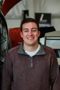 Portrait of young man smiling at Hall's Sport Center, sporting equipment and sports gear in background.