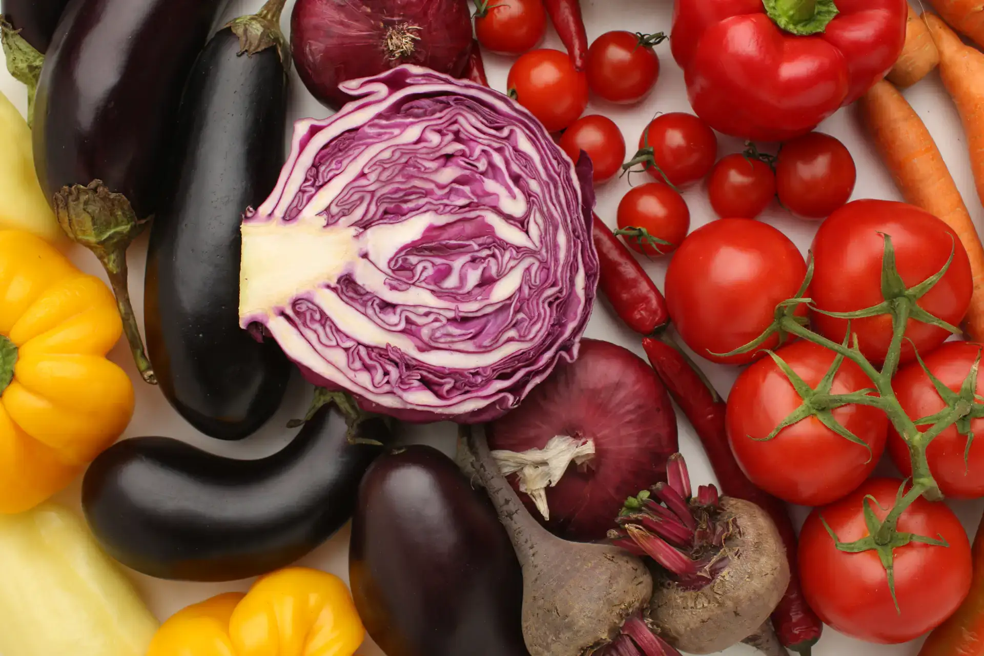 Colorful fresh vegetables including eggplant, tomatoes, carrots, and purple cabbage.