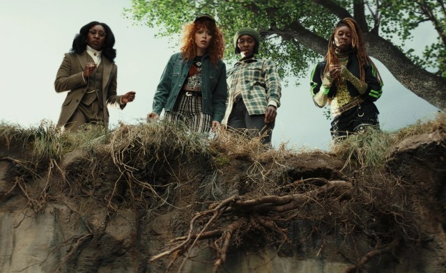 Four women, three of whom are identical, peering over the ledge of a cliff with looks of dismay on their faces.