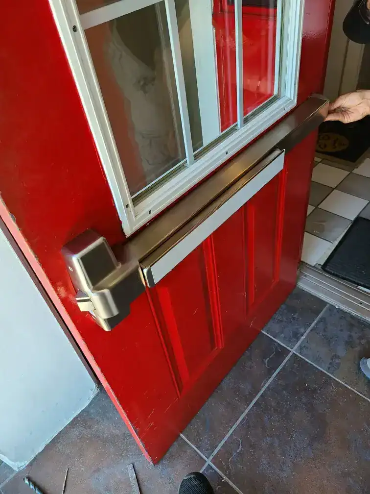 Commercial locksmith installing panic bar exit device on red storefront door in Laurel MD for code compliant business security and access control.