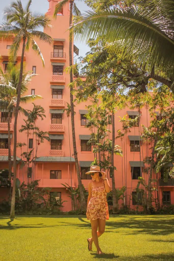 girl standing in front of a pink hotel holding onto her hat