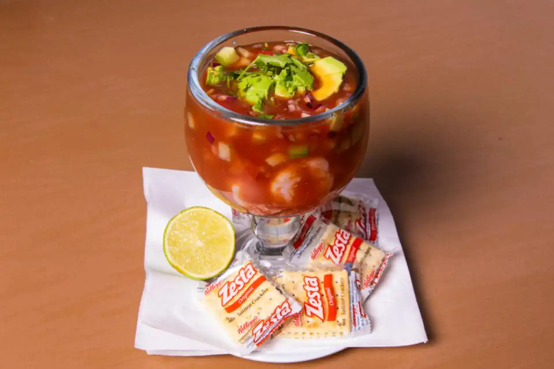 Clamato cocktail with lime, snacks, and fresh ingredients on a wooden table.