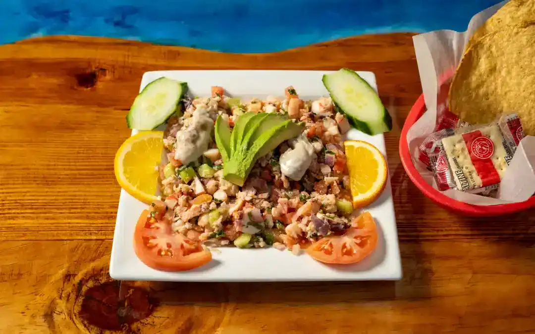 Seafood ceviche with cucumber, tomato, and lemon slices on a white plate.