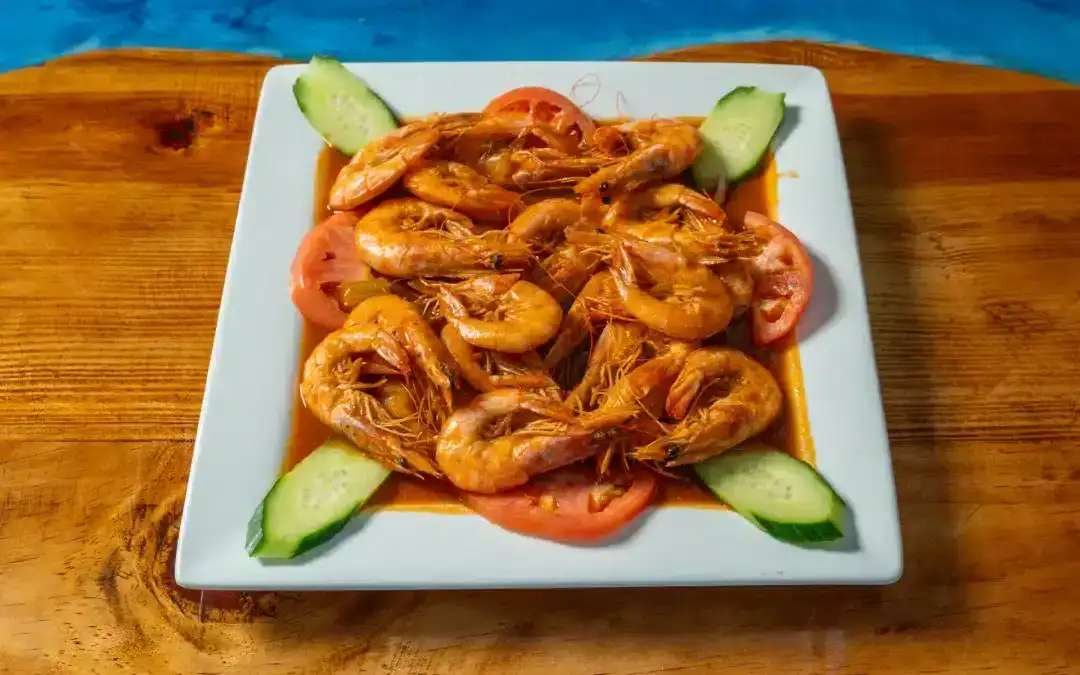 Spicy shrimp dish with cucumber and tomato slices on a white plate.