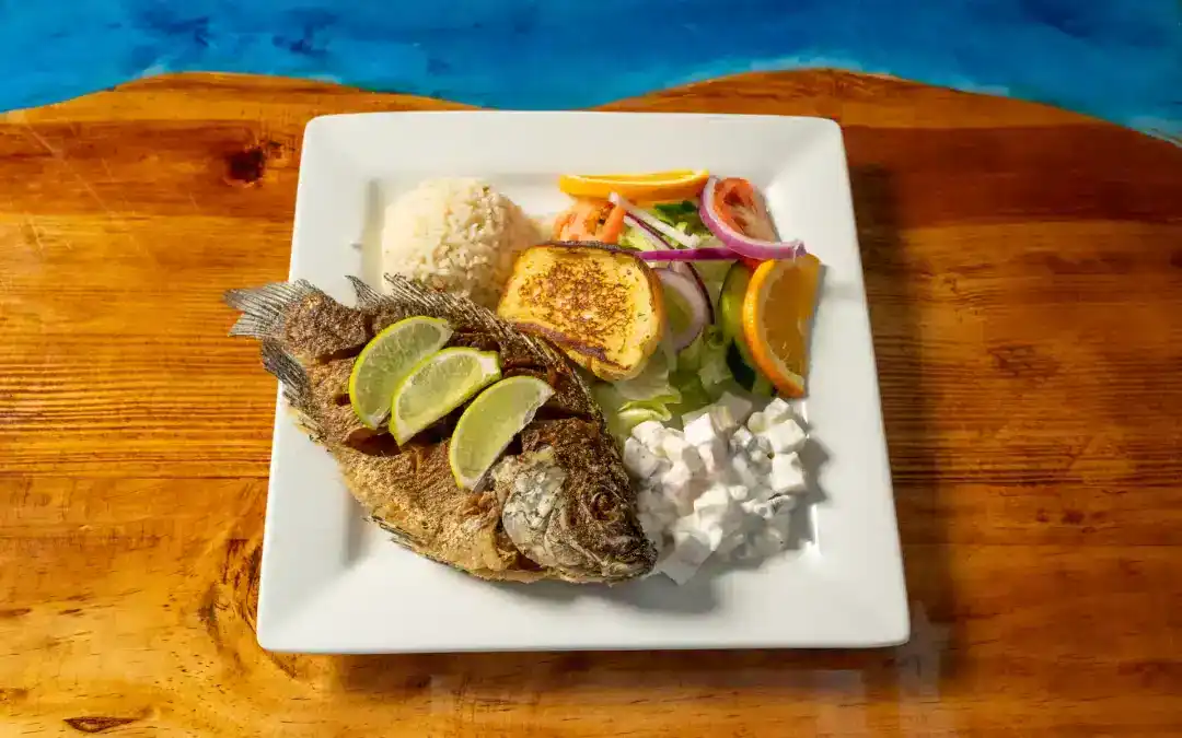 Fresh whole mojara fish served with lime, rice, and vegetables on a white plate.