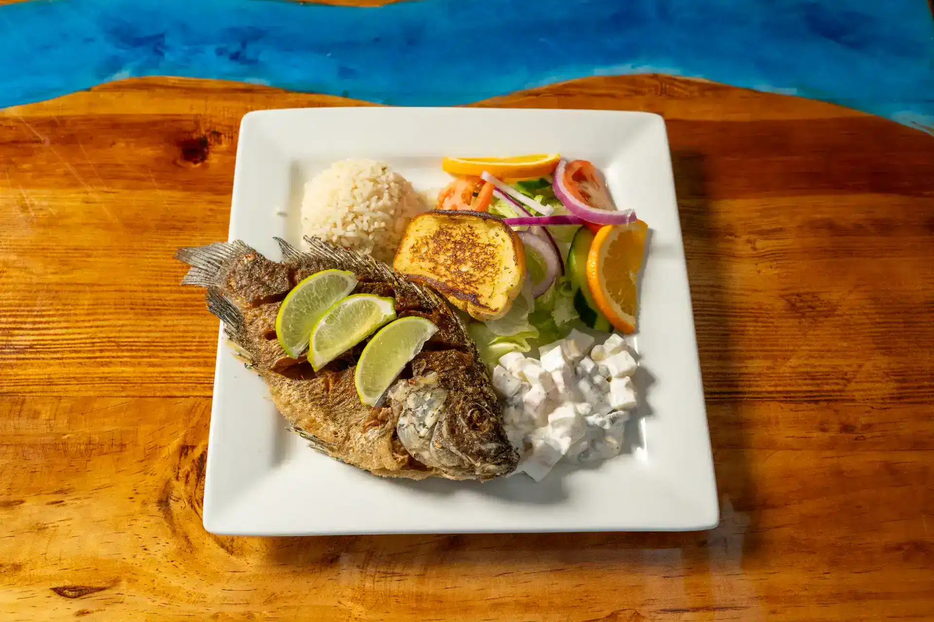 Fresh whole mojara fish served with lime, rice, and vegetables on a white plate.