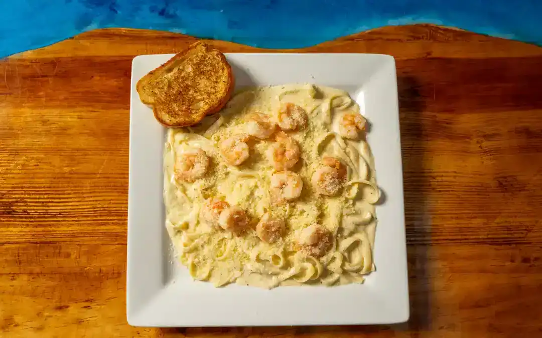 Creamy shrimp Alfredo pasta served with garlic bread on a white plate.