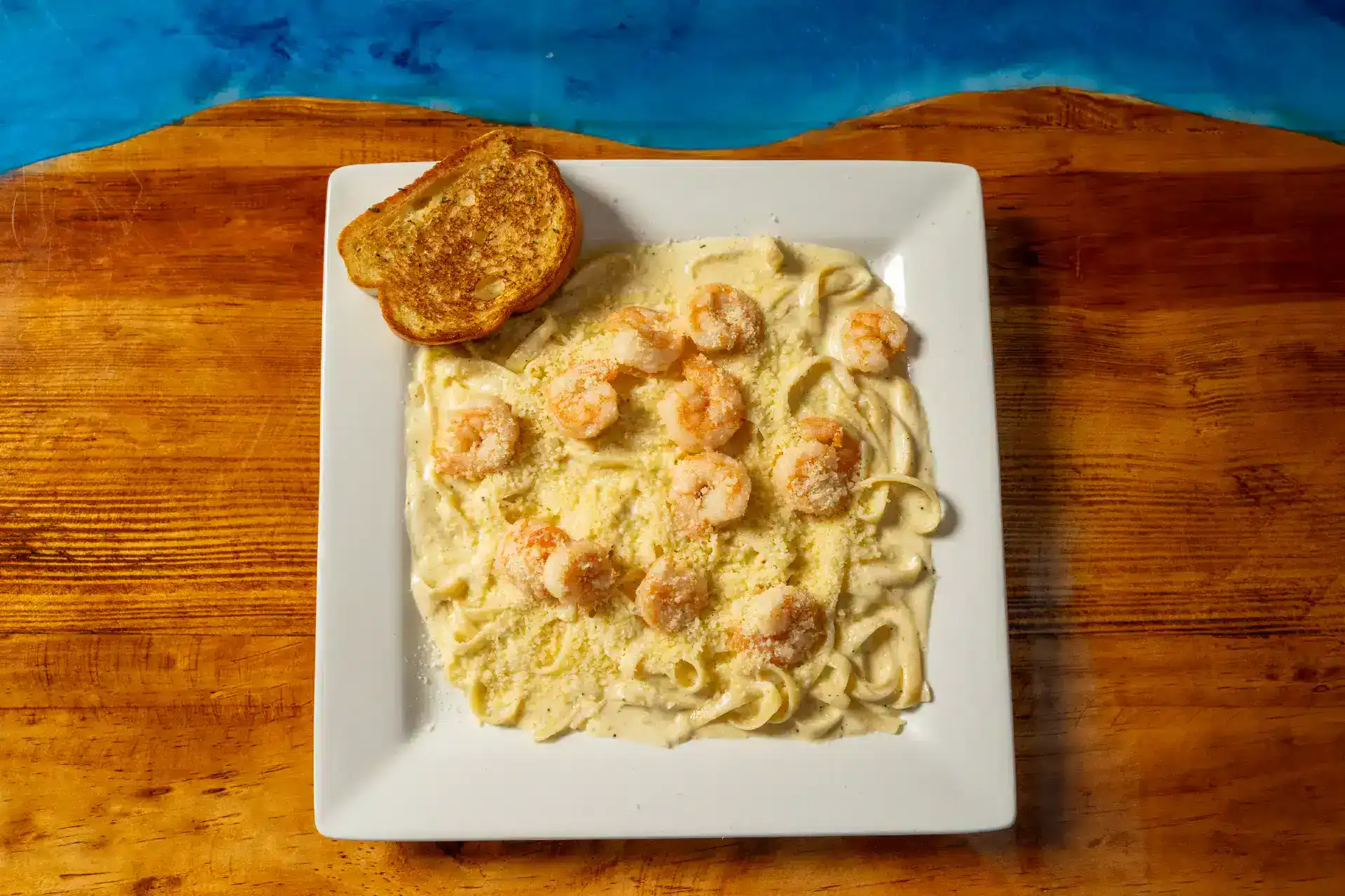 Creamy shrimp Alfredo pasta served with garlic bread on a white plate.