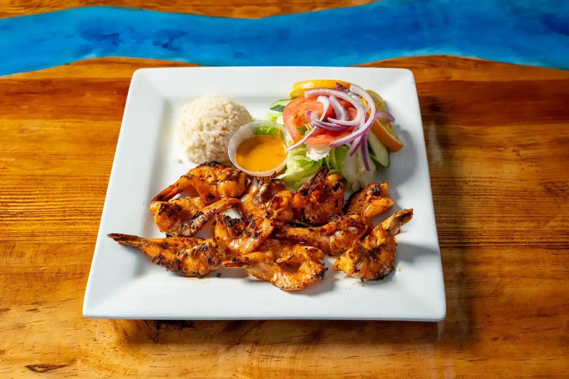 Grilled shrimp with salad, rice, and dipping sauce on a white plate.