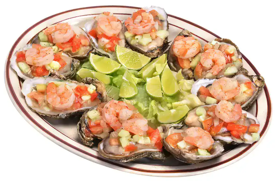 Oysters topped with shrimp, vegetables, and lime wedges on a serving platter.