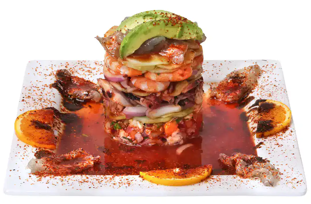 Seafood tower with avocado and sauce on a white plate.