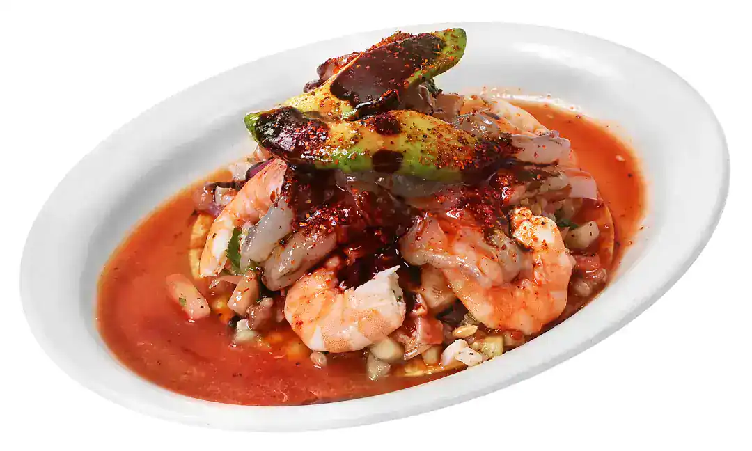 Tostada Buchona with shrimp, avocado, and spicy sauce on a white plate.