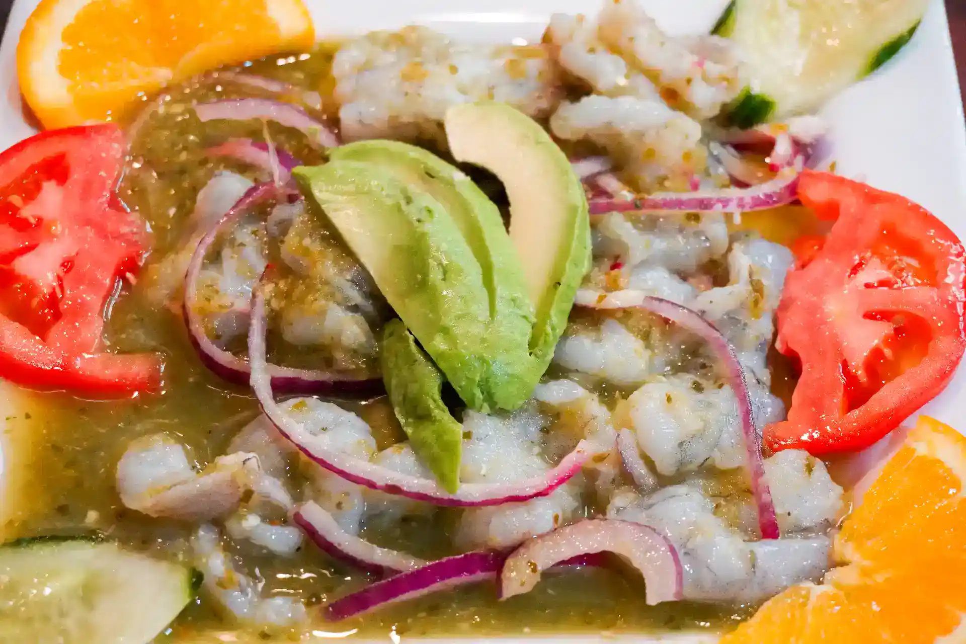 Ceviche dish with avocado, tomatoes, onions, and citrus slices.