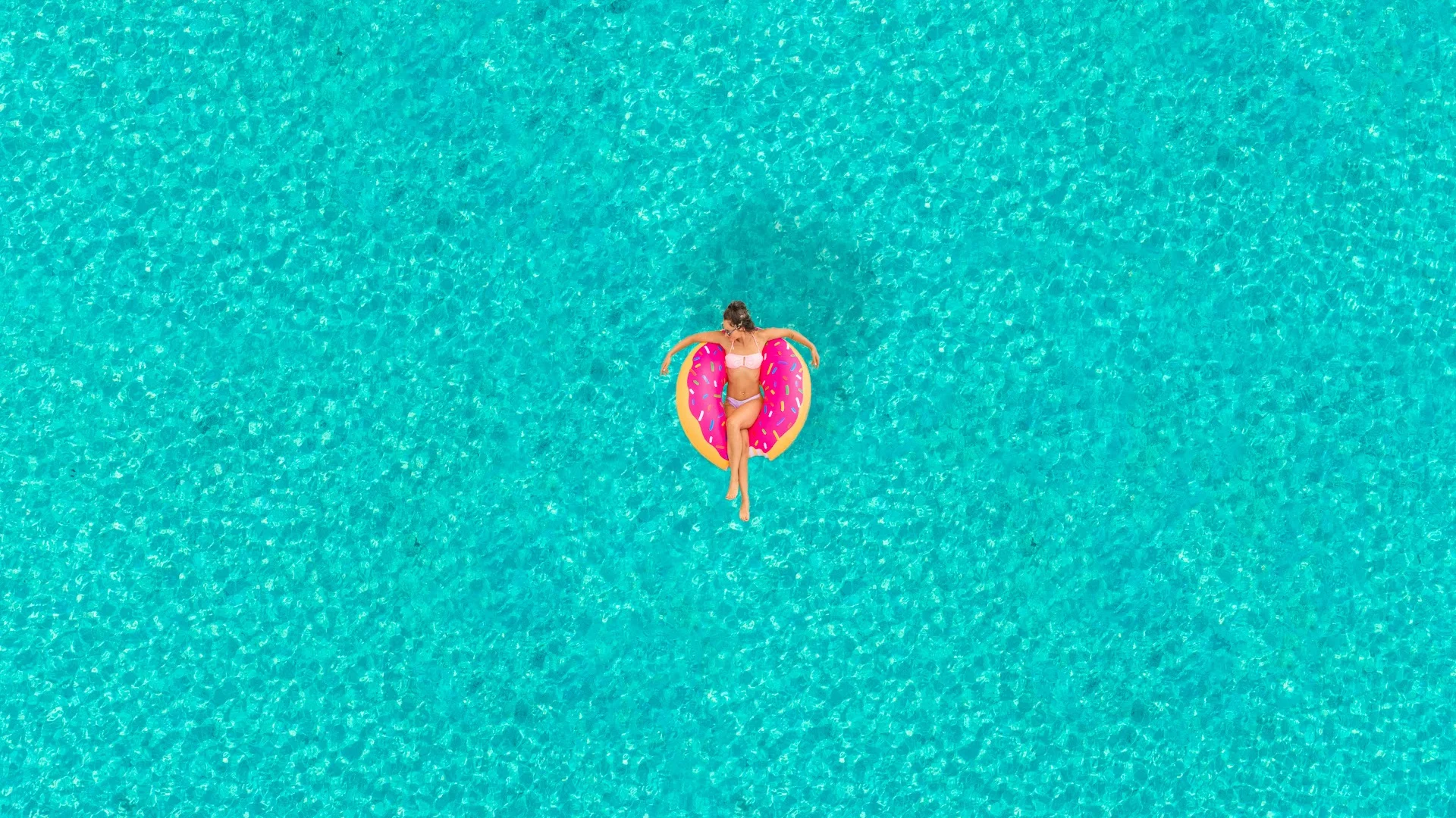Woman on a hot pink donut inflatable floating in the sea as per our 100 self-care ideas