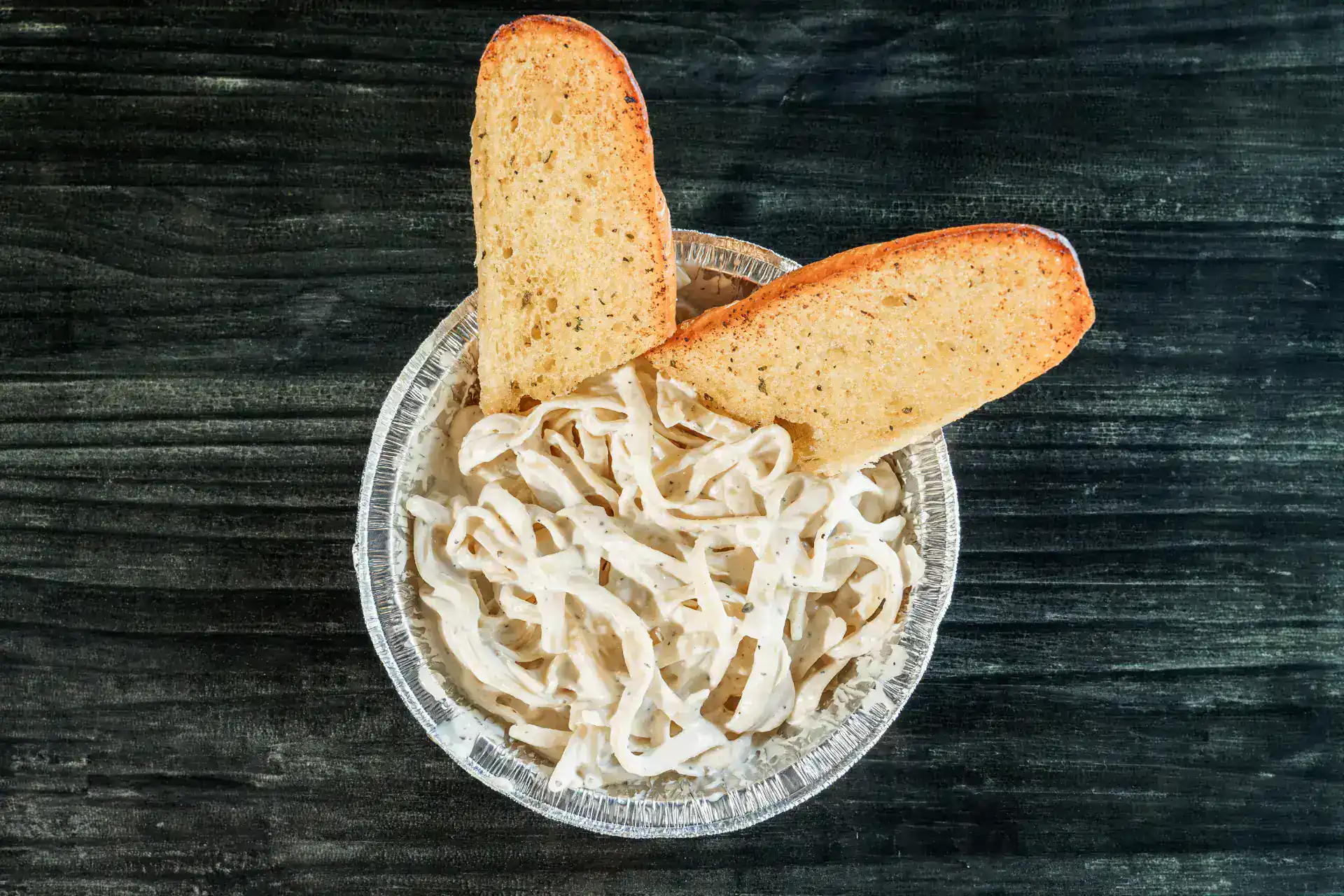 Creamy Alfredo sauce with breadsticks in a glass bowl on dark wood.