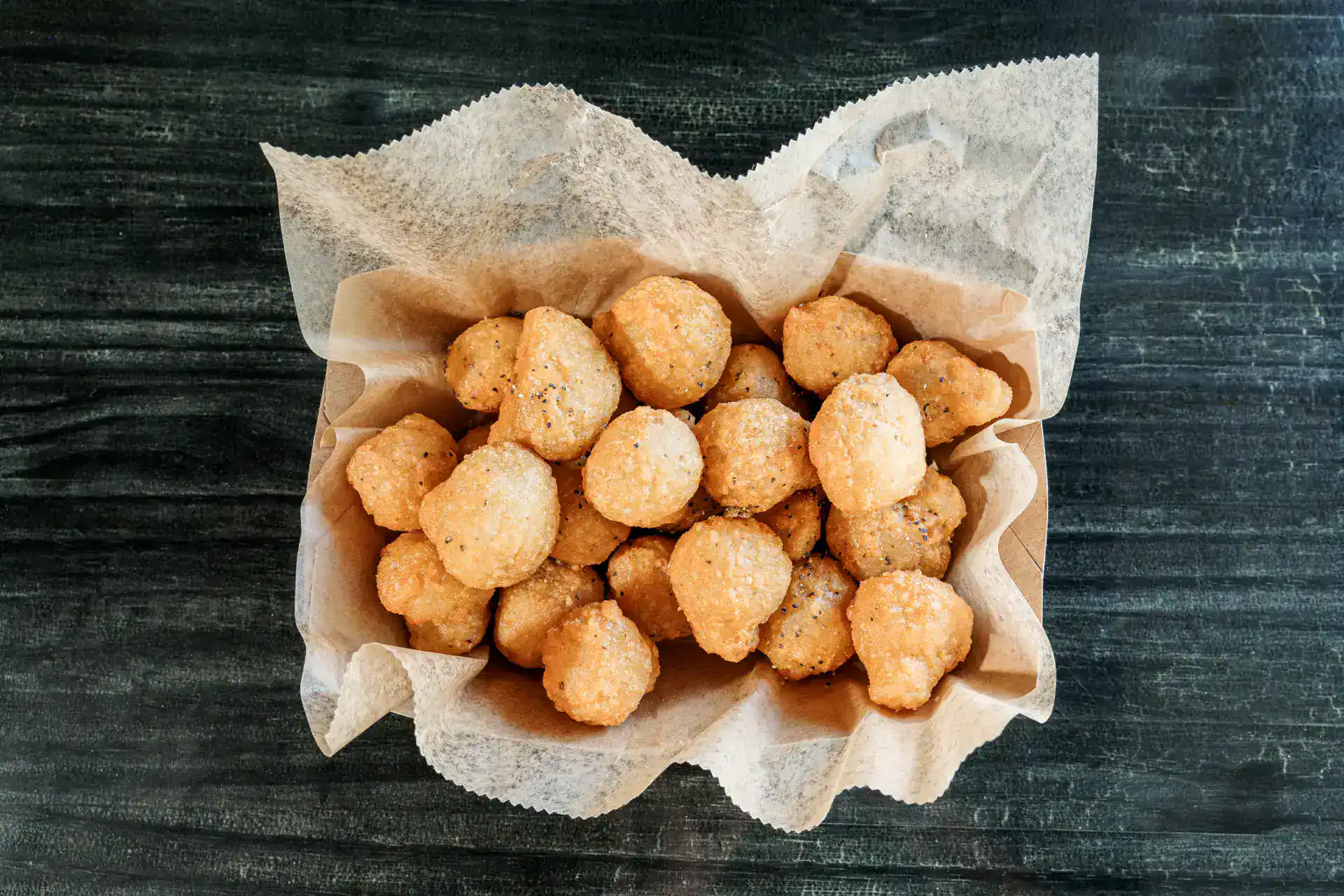 Crispy fried mushrooms served in a paper-lined basket on a dark wooden table.