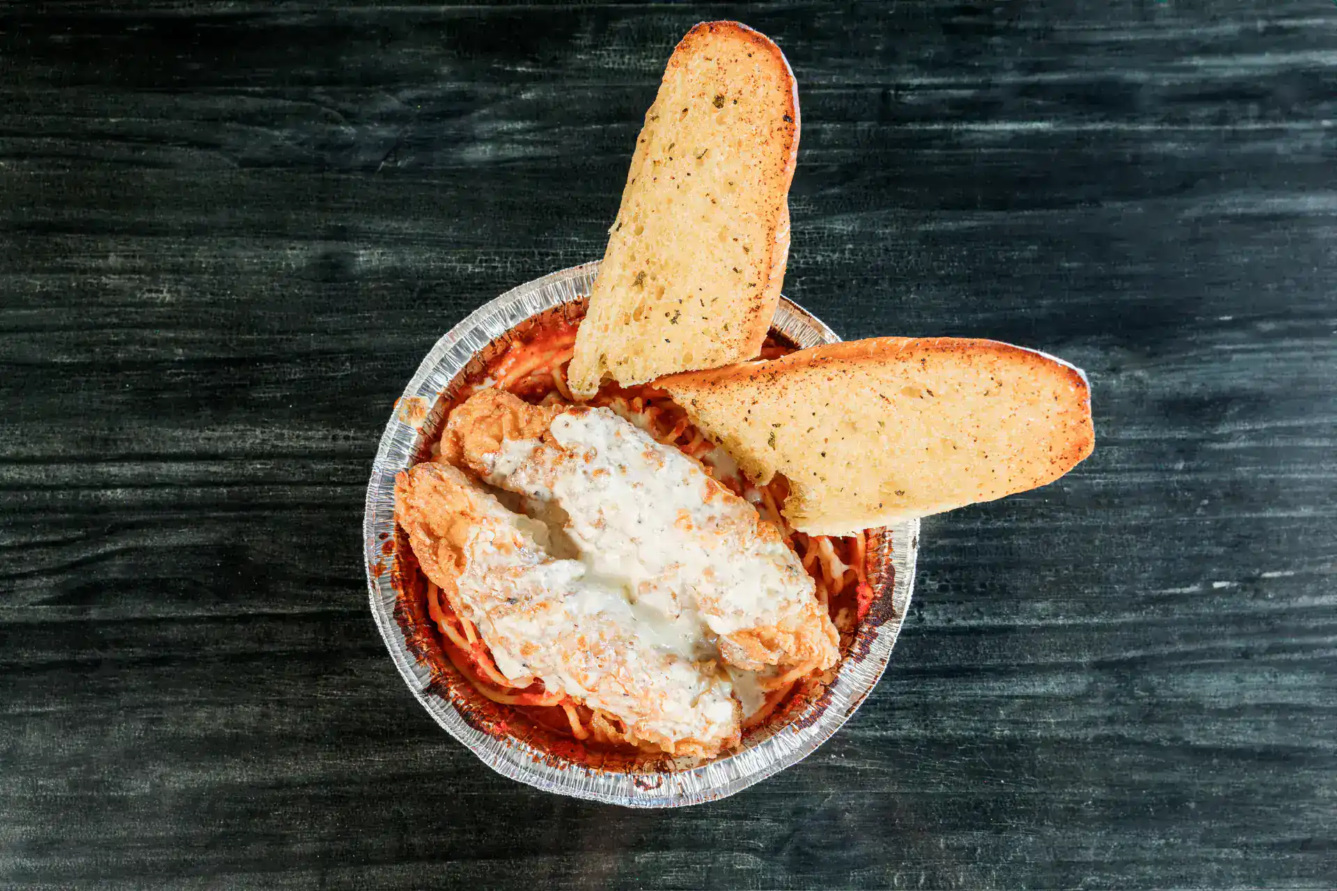 Chicken Parmesan served with garlic bread slices on a dark table.