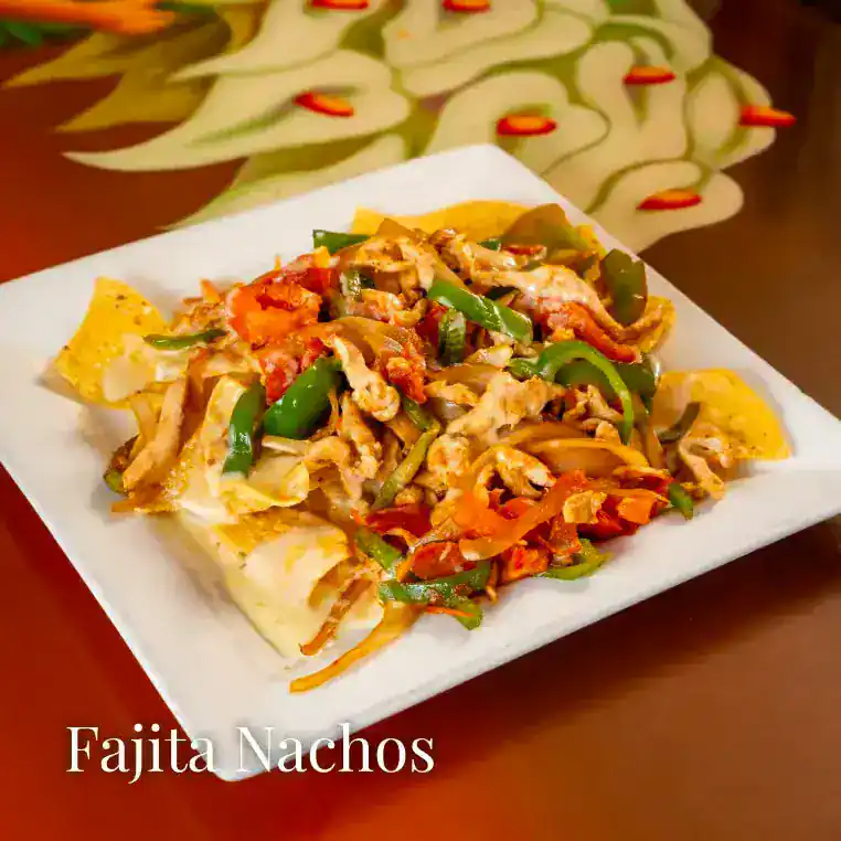 Tasty fajita nachos with peppers, chicken, and cheese on a white plate.