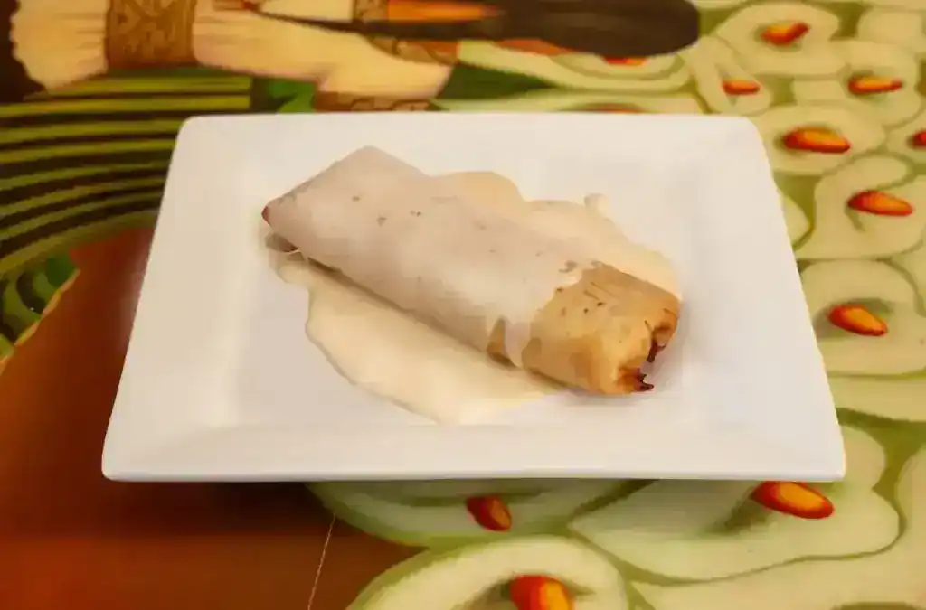 Delicious spring roll with creamy dipping sauce on a white plate.