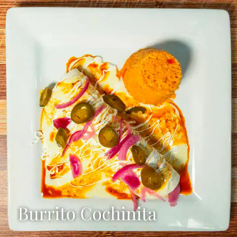 Delicious Cochinita Burrito with pickled onions and olives on a white plate.
