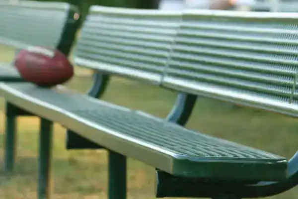 Green metal park bench with a football on it, outdoors in a park setting.