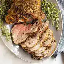 Juicy roasted beef slices garnished with herbs on a white plate.
