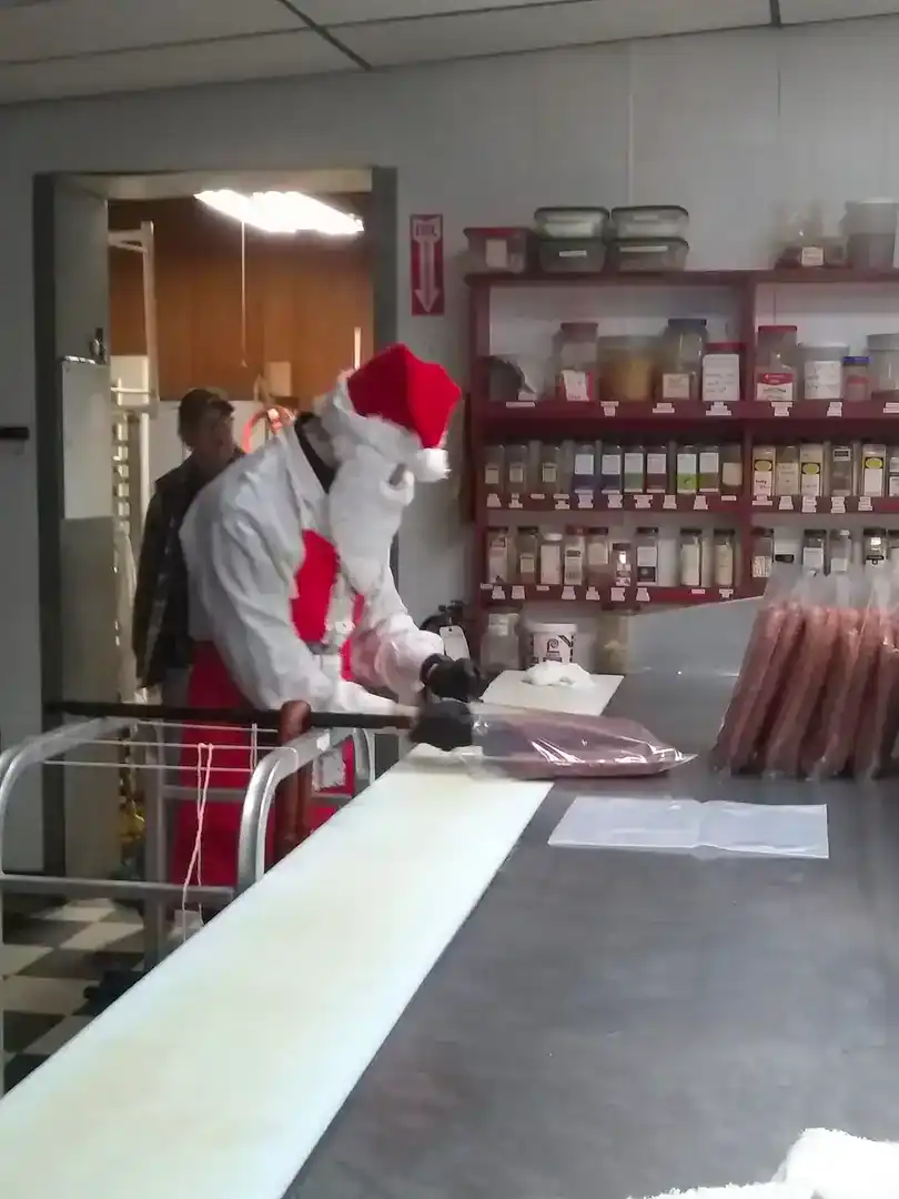Worker dressed as Santa Claus preparing meat in a grocery store.