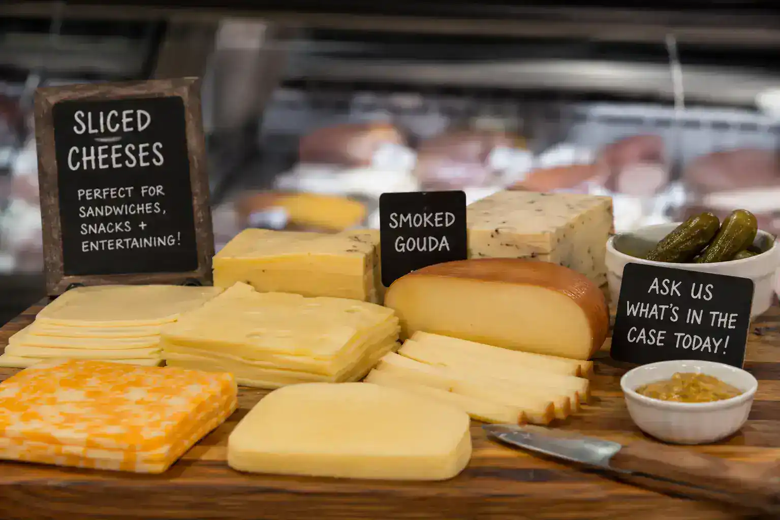 Assorted cheeses, smoked gouda, and pickles on a wooden platter for tasting.