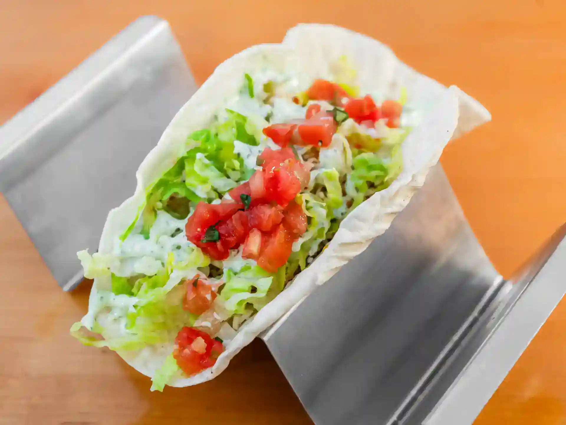 Fresh taco with lettuce, tomato, and cheese on a metal taco holder.