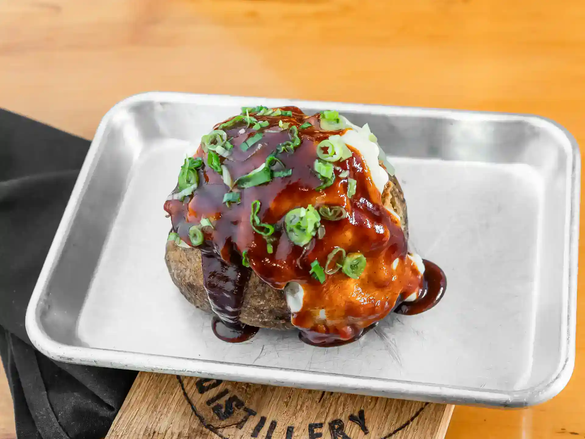 Gourmet potato skins topped with cheese, green onions, and barbecue sauce on a metal tray.
