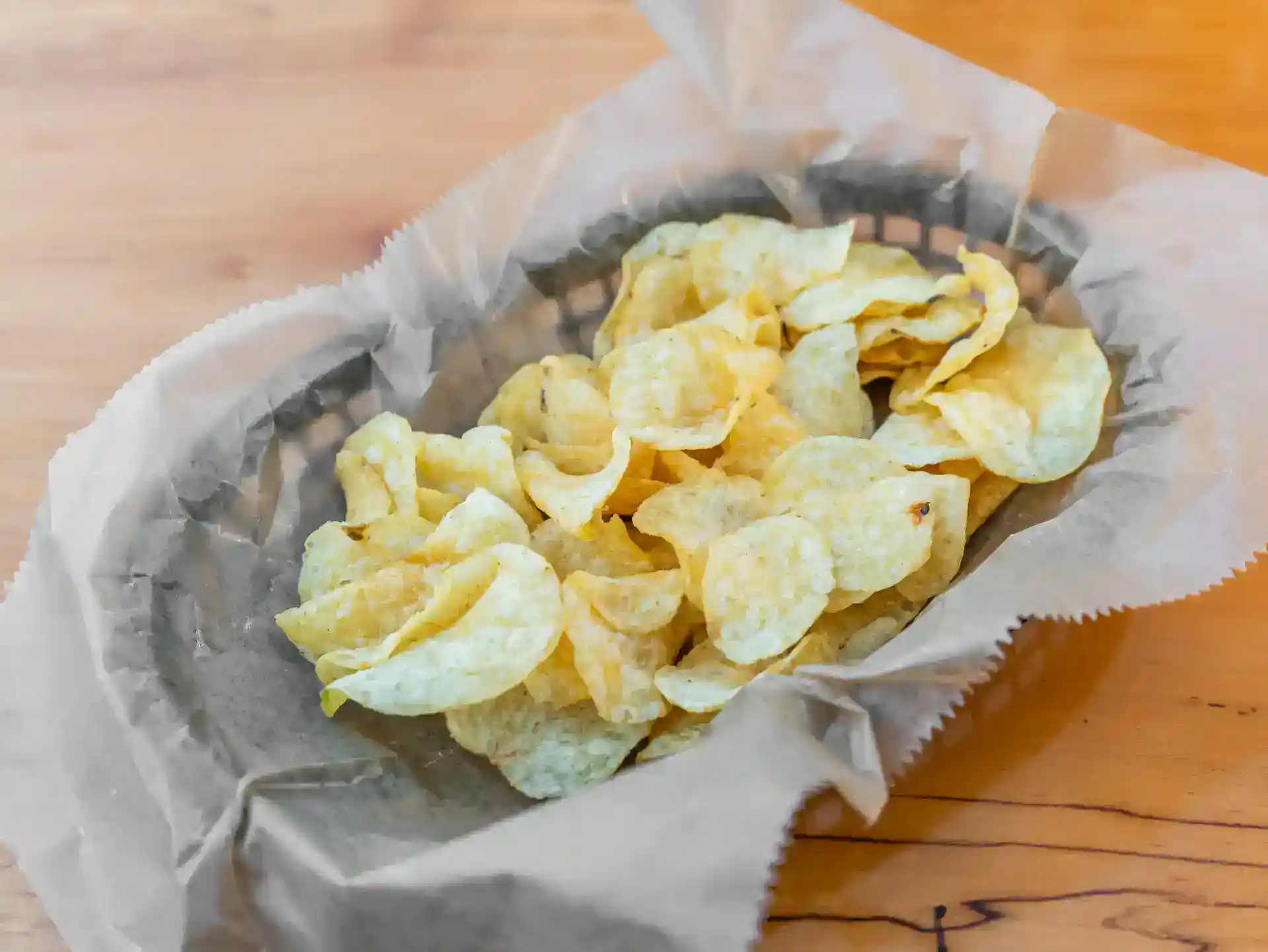 Potato chips in a paper bag on a wooden surface.