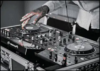 A person operates a Pioneer DJ controller, adjusting knobs and spinning a jog wheel while wearing headphones.