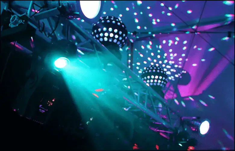 Stage lights and spotlights shine blue and purple beams, reflecting off disco balls and creating patterns on the ceiling.