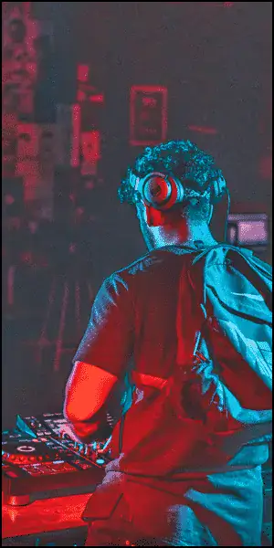 Person wearing headphones stands at a DJ console with red and blue lighting, facing away from the camera.