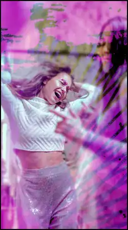 Two women dance and smile in a room, with a pink and purple overlay effect partially obscuring the image.