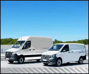 Two white Mercedes-Benz cargo vans are parked side by side on a paved area under a clear blue sky.