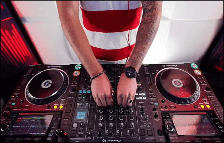 A person operating a professional DJ controller with both hands, surrounded by colorful lights and audio equipment.